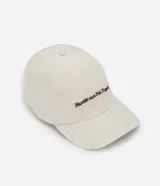 Gorra de algodón color beige con visera curva, ojales de ventilación y detalle de bordado con texto en tono marrón.
