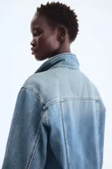 Campera de denim de algodón rígido, color azul, con cuello clásico y cierre frontal de botones metálicos. Cuenta con bolsillos superiores con solapa y botón, bolsillos laterales insertados y puños abotonados.