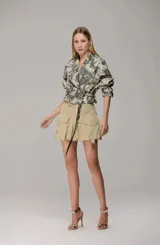 Chaqueta corta de estilo militar con estampado camuflado en tonos grises y verdes. Presenta solapas clásicas, mangas largas con puños ajustables y un cinturón integrado con hebilla metálica que permite entallar la cintura.