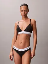 Bralette Calvin Klein de corte triangular, color negro con estampado geométrico de monogramas y banda elástica inferior blanca con el logotipo de la marca. Cuenta con tirantes finos ajustables.