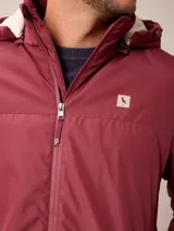 Campera de nylon gris con capucha, cierre frontal completo y bolsillos laterales. Presenta un diseño minimalista con logo bordado en el pecho.