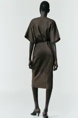 Vestido midi de tejido piqué en color marrón oscuro jaspeado, con escote en pico cruzado y mangas cortas. Presenta detalle de frunces en la cintura y un cinturón integrado con hebilla metálica a contraste.