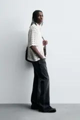 Camisa negra de corte relajado con tejido semitransparente de estructura abierta y patrón a cuadros. Presenta cuello solapa, manga corta, bolsillo plastrón en el pecho y cierre frontal de botones.