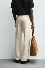 Pantalón de algodón color beige claro, de corte recto (regular fit), con pespuntes en hilo contrastante oscuro. Presenta bolsillos delanteros y bolsillos traseros de parche.