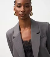 Blazer corto de sastrería color gris oscuro, con solapas estructuradas, manga larga y corte ajustado. Se combina con un top de encaje negro y pantalón ancho a juego.