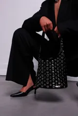 Cartera tipo hobo de PU acharolada color negro, cubierta de tachas plateadas.