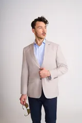 Blazer de corte clásico color beige, con solapas de muesca, cierre frontal de dos botones y bolsillos laterales con solapa.