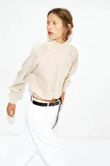 Blusa marrón de punto fluido, con cuello subido abotonado en un lateral y mangas largas con puños ajustados. Presenta un diseño fruncido en la parte frontal que aporta volumen.