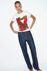 Camiseta de algodón color marrón oscuro, de corte regular, cuello redondo y manga corta. Presenta una estampación metalizada dorada en el parte frontal con texto "REYKJAVIK ART GALLERY" y "ABSTRACT MOVEMENTS Reykjavik, Iceland, 1975".