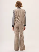 Chaqueta estilo bomber con diseño híbrido, combinando mangas y frente en tejido de lana con patrón de espiga en tonos tierra, y espalda en tejido liso de poliéster color marrón. Presenta puños y ruedo elásticos en color negro, brindando una estructura definida y un estilo contemporáneo.