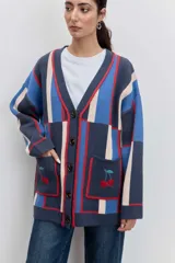 Cardigan de punto con diseño de bloques de color en azul, rojo y crema. Presenta cuello en V, cierre frontal con botones, mangas largas y dos bolsillos delanteros con bordado de cerezas.