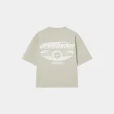 Camiseta beige de corte "boxy fit" con estampado blanco en la espalda que incluye el texto "emestudios" y un diseño gráfico con estrellas y texto adicional.