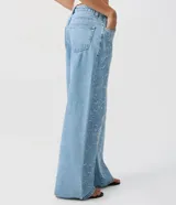Pantalón wide leg de jean celeste con talle medio y bordados florales en hilo celeste claro a lo largo de las piernas. Cuenta con bolsillos funcionales, pasadores para cinto y cierre frontal con botón y cremallera.