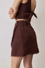 Falda cruzada tipo wrap color beige, de lino, con diseño asimétrico y bordes deshilachados. Cuenta con cierre de botón en la cintura.