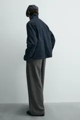 Chaqueta de denim de algodón en color azul oscuro, con cuello solapa y manga larga. Presenta cierre frontal con cremallera oculta bajo una solapa con alamares metálicos, bolsillo de vivo en el pecho y bolsillos de plastrón con solapa en la cadera.