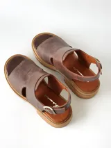 Sandalias de cuero color chocolate con suela track y taco bajo cuadrado. Poseen capellada cerrada con aberturas laterales y tira ajustable en el talón con hebilla metálica.