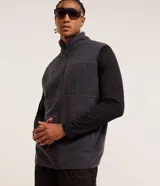 Chaleco deportivo gris oscuro con cuello alto y cierre frontal con cremallera. Presenta recortes en tejido liso en la parte superior del pecho y en los bolsillos laterales.