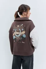 Cardigan de punto con diseño bicolor, cuerpo en color marrón y mangas largas en color crema con textura trenzada. Presenta cuello polo, cierre frontal con cremallera y puños acanalados.