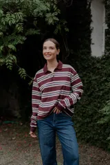 Remera de manga larga con cuello polo y cierre frontal de botones. Presenta un diseño a rayas horizontales en tonos bordó, blanco y celeste.