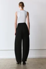 Pantalón negro de tiro alto, con pliegues en el delantero y bolsillos laterales ocultos. Cierre frontal con cremallera y ganchos metálicos.