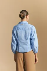 Camisa azul a rayas blancas, de manga larga con puños elastizados, entallada en la cintura y con cierre de botones frontales.