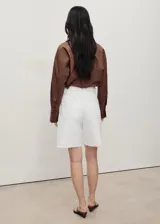 Short de denim blanco de tiro medio, diseño de corte recto y cinco bolsillos, con trabillas para cinturón y bajo deshilachado.