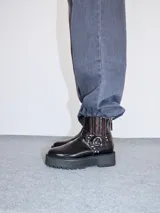 Bota corta de cuero negro tipo biker, con suela track de goma, plataforma, costuras y bordados decorativos en hilo rojo. Presenta tiras con hebillas metálicas y cierre en la parte trasera.