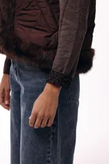 Chaleco acolchado color marrón con terminaciones de piel sintética en los bordes y cuello, aportando volumen y textura.