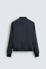 Cazadora bomber ligera de tejido técnico color verde oliva, con cuello, puños y bajo en rib elástico. Presenta cierre frontal de cremallera y bolsillos de vivo en la cadera.