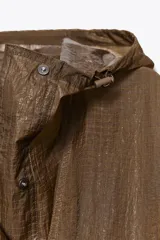 Chubasquero tipo capa oversize con capucha ajustable, manga larga y cierre frontal con botones a presión. Presenta un diseño con bolsillos delanteros y bajo asimétrico con aberturas laterales.