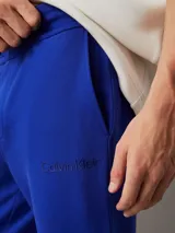 Pantalón de chándal azul eléctrico de felpa de algodón regenerativo, con cintura elástica con cordón, puños de canalé, bolsillos laterales y trasero, y logo de Calvin Klein en relieve en la cadera.