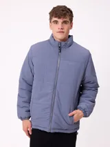 Campera reversible de nylon con cuello alto y cierre frontal. Un lado es de color gris liso con logo bordado, mientras que el otro lado presenta un estampado abstracto en tonos azules. Cuenta con bolsillos laterales y puños elásticos.