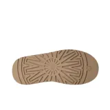 Zuecos UGG modelo Tazz de gamuza color beige, con plataforma alta y detalle de costura trenzada en el borde superior. Presenta el logo de la marca grabado en el lateral.