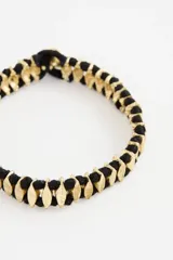 Pulsera de diseño étnico con eslabones metálicos dorados entrelazados con hilo de algodón negro, creando un patrón geométrico.