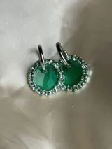 Aros colgantes con forma circular, hechos de resina color lila y borde de strass plateado. El aro es de acero quirúrgico plateado.