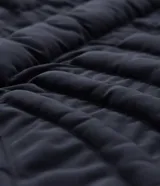 Campera puffer negra con diseño acolchado que simula una estructura de esqueleto. Cuenta con capucha, cierre frontal con cremallera, mangas largas y puños elásticos.