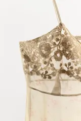 Top de tirantes finos confeccionado en organza semitransparente con estampado floral sutil. Presenta escote en pico con aplicaciones de bordados florales a contraste y terminación en puntilla en el bajo.