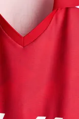 Camiseta de futbol de manga corta de la marca Lotto, en color rojo con un sutil estampado geométrico. Cuenta con cuello tipo polo abierto con escote en V y un calce holgado. Las mangas presentan una franja blanca lateral decorada con el logo de la marca repetido. El logotipo de Lotto destaca en blanco en el centro del pecho.