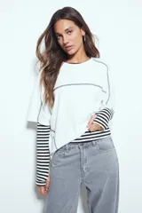 Remera de manga corta con silueta relajada y costuras a la vista en color blanco que contrastan sobre el tejido negro. Presenta un diseño moderno con terminaciones destacadas.