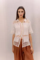 Camisa de algodón color crudo, con cuello camisero, mangas cortas y cierre frontal con botones. Presenta paneles de tejido calado y detalles bordados transparentes.