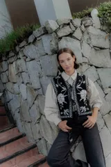 Chaleco tejido de punto con diseño floral en contraste, cierre frontal con lazos y terminaciones con guardas geométricas.