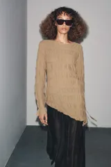 Top de manga larga color beige, con textura fruncida en todo el cuerpo y mangas. Presenta cuello redondo y bajo asimétrico con aberturas laterales ajustables con cordones.