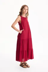 Vestido largo fluido de lino color rojo, sin mangas, con escote redondo, bolsillos laterales y falda escalonada con volados.