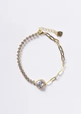 Pulsera de diseño mixto con una mitad de cadena de eslabones gruesos y otra mitad de engarces con zirconias, unida por un dije central en forma de corazón con zirconia grande. Fabricada en plata 925 con baño de oro 18k.
