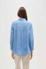 Camisa de manga larga color celeste, con cuello camisero y cierre frontal de botones. Presenta un diseño distintivo con paneles de encaje tipo crochet en la parte superior delantera.