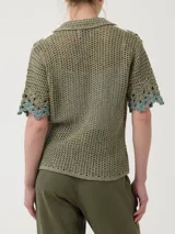 Sweater tejido a crochet color verde oliva, con cuello camisero, cierre frontal con botones y mangas cortas. Presenta bordados de flores blancas y celestes en el frente.