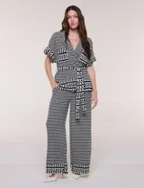 Conjunto de dos piezas de calce fluido y relajado con estampado geométrico en blanco y negro. Incluye una chaqueta con escote en V, solapa, diseño cruzado con lazo y bolsillos con solapa en el pecho, y un pantalón de tiro alto y corte wide leg.