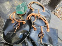 Cartera grande de cuero negro con textura símil cocodrilo, asas de mano y hombro de cuero tostado, costuras artesanales visibles y detalle decorativo de guampa en el frente.