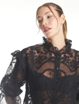 Blusa de tul bordado color negro, con cuello alto, cierre frontal con botones y mangas tres cuartos con terminación amplia.