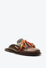 Zueco mocasín de cuero marrón, con taco plano, hebilla metálica dorada lateral y detalle de cordón naranja con cuentas decorativas en el empeine.
